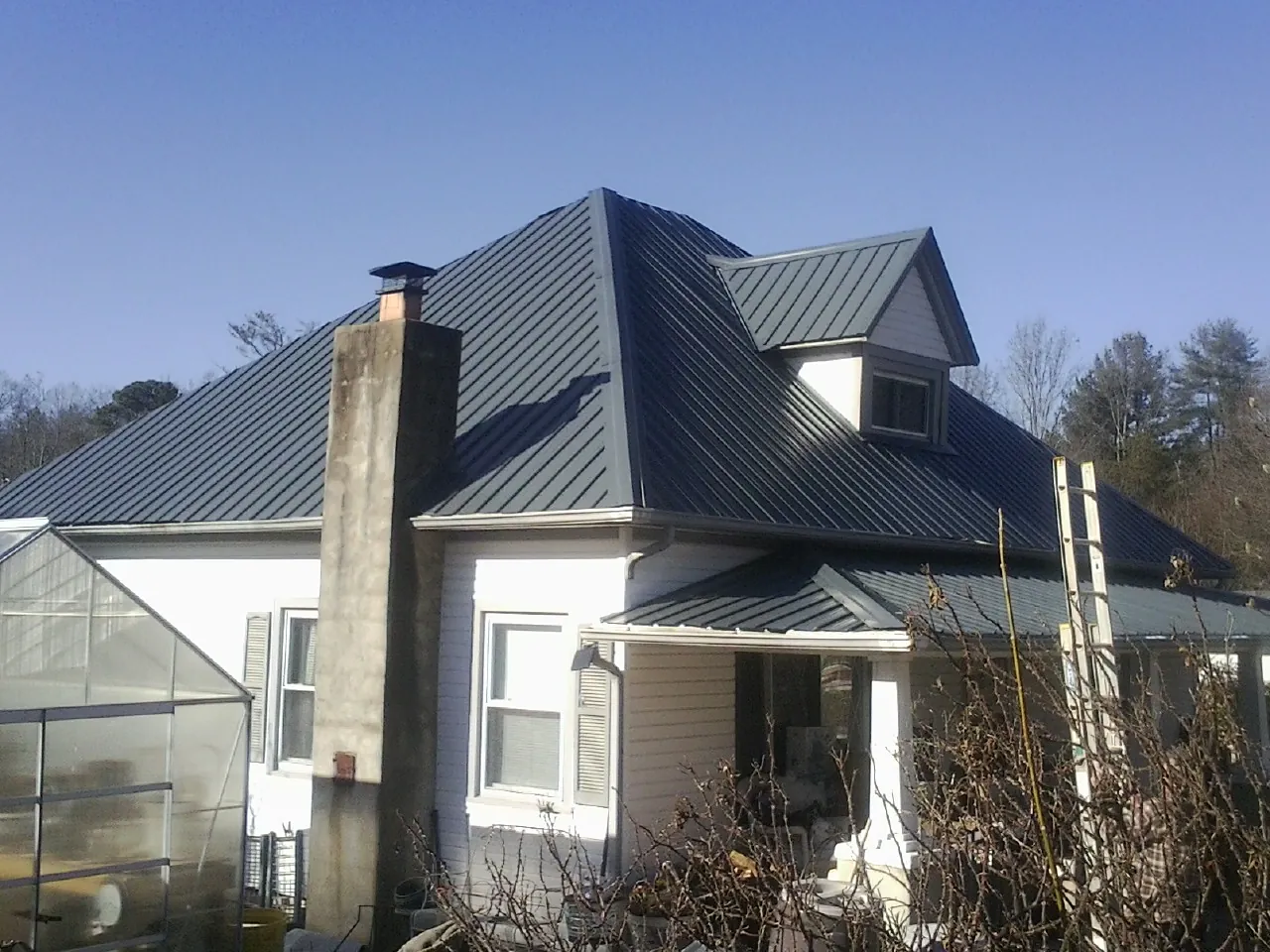 Dark blue standing seam metal roof on a white farmhouse with dormer — Slate & Tile Roof Repair by Roofing Brothers in Coleharbor