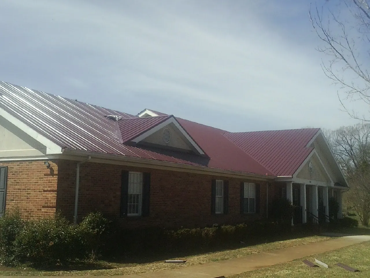 Red metal roof with gabled entries on a long brick building, from a Hail Damage Roof Repair job in Coleharbor
