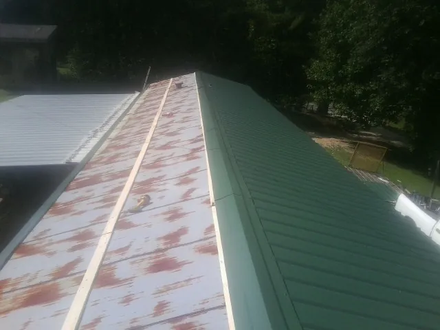 Old rusted panels beside newly installed green metal roofing — Wind Damage Roof Repair by Roofing Brothers in Coleharbor