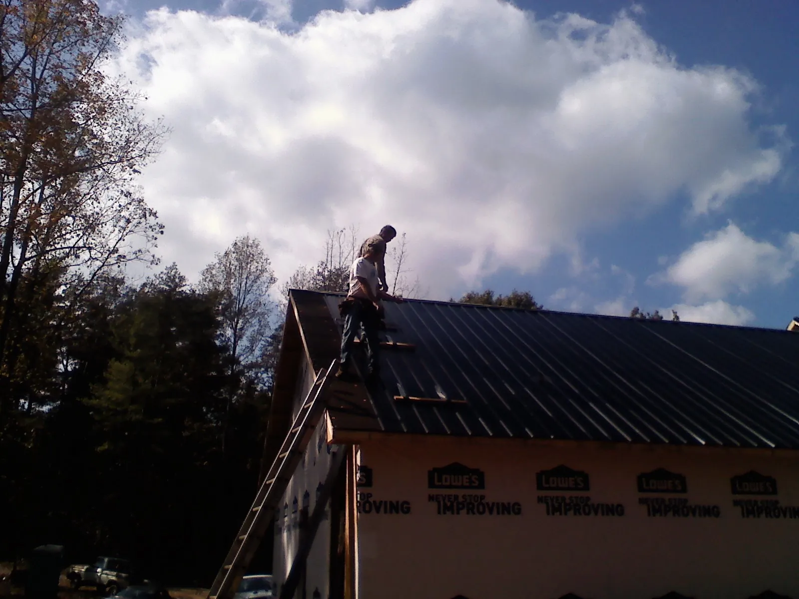 Roofer fastening dark metal panels high against a cloudy sky, from a Roof Inspection job in Coleharbor