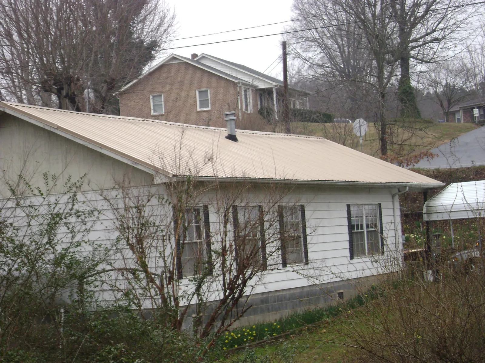 Tan metal roof on a white sided house set into a hillside — Commercial Roofing by Roofing Brothers in Coleharbor