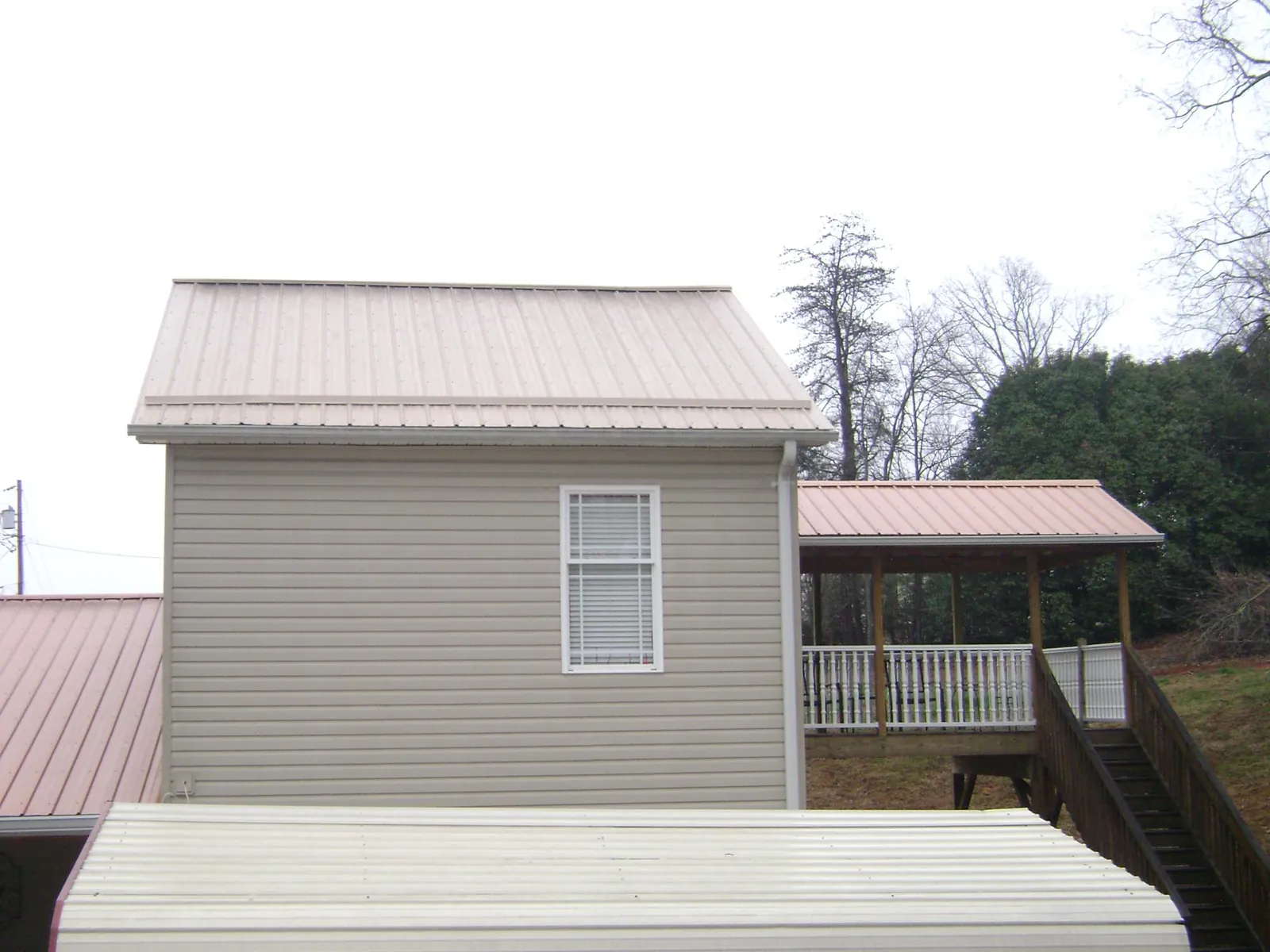 Tan metal roofs on a two story addition and attached porch, from a Roof Replacement job in Coleharbor